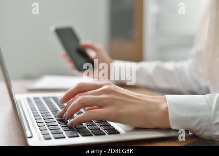 Close up of young female hands typing on the keyboard and making a call on a smartphone Stock Photo