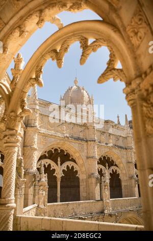 Ornate Manueline architecture and arches with a view of the domed bell tower in the cloister of Jerónimos Monastery in Lisbon, Portugal, Europe.