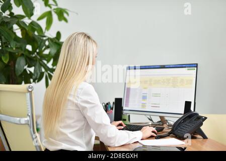 Young blonde woman in white blouse works at a desktop computer in the office Stock Photo