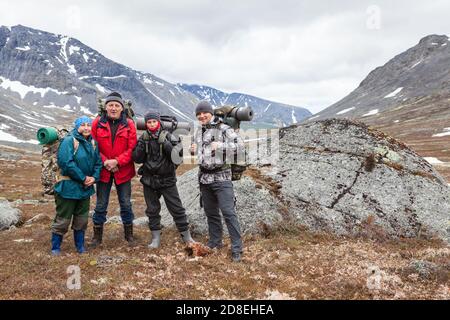 Team of Caucasian hikers with backpacks, different ages four mountaineers standing in mountain valley, portrait with copy space Stock Photo