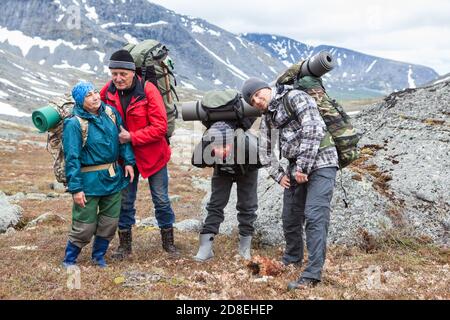 Tired backpackers with heavy backpacks standing in mountains, four mountaineers portrait of different ages Stock Photo