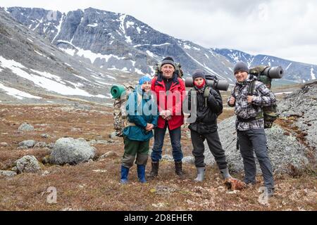 Team of Caucasian hikers with backpacks, four people standing in mountain valley, portrait with copy space Stock Photo