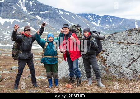 Mountaineers cheering and greeting with hands up, group of Caucasian hikers from one family hiking with backpack in mountains Stock Photo