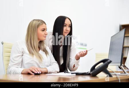 Two young women office workers are discussion and looking at the monitor Stock Photo