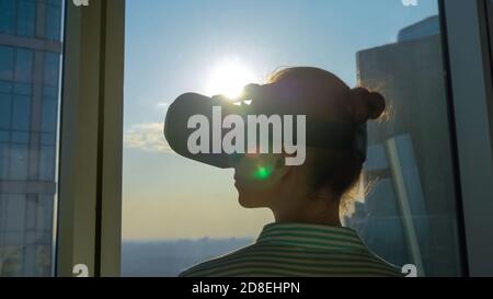 VR, sightseeing, discover, technology concept. Woman using virtual reality headset and looking around against view on cityscape from panoramic Stock Photo