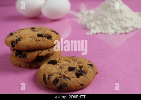 kitchen cooking process homemade chocolate cookies with chocolate drops in the background flour and chicken eggs lie on a pink fuchsia mirror backgrou Stock Photo