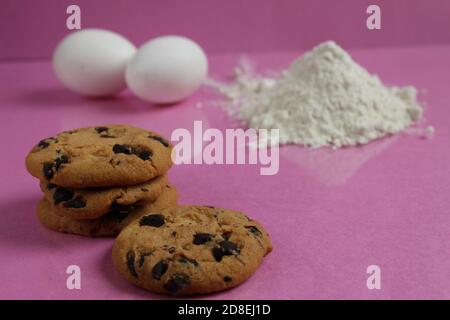 kitchen cooking process homemade chocolate cookies with chocolate drops in the background flour and chicken eggs lie on a pink fuchsia mirror backgrou Stock Photo