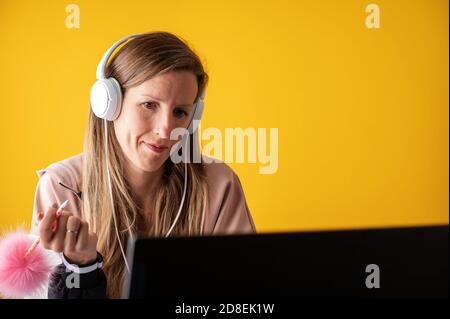 Young woman, student, studying from home listening to webinar with headphones on her. Stock Photo