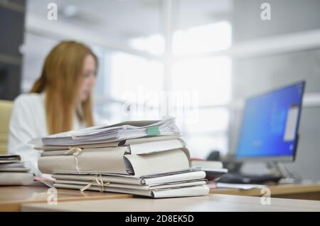 A large stack of papers in the office lies on the desk of a busy woman office manager Stock Photo