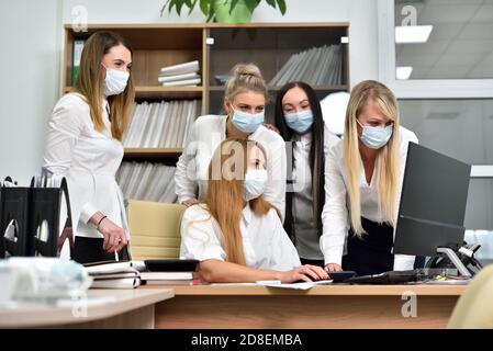 Female office managers in face masks at a meeting in the office discussing a new project using a computer Stock Photo