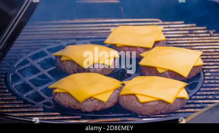 Process of cooking fresh meat cutlets and yellow cheese for cheeseburgers on grill at summer local food market - close up view. Outdoor cooking Stock Photo
