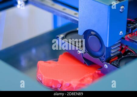 3D printer prints physical red 3D model with plastic wire filament at modern technology exhibition, factory - close up. Additive technology, science Stock Photo