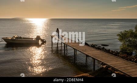 Lonely young woman sitting on a pier, relaxing and enjoying the sunset at Razim lake, Romania Stock Photo