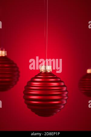 Horizontally ribbed Christmas balls hanging against burgundy red background. Christmas decoration, festive atmosphere concept. Selective focus, portra Stock Photo