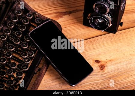 A mobile phone leaning upon an old broken typing machine with an analogical camera next to it Stock Photo