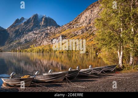 Boats lined up on the shore of a lake in the Sierra Nevada mountains with fall colors reflecting in the water. Stock Photo