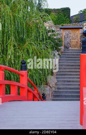 Arched wooden red footbridge and stone steps of stairway leading up to the temple gate. Stock Photo