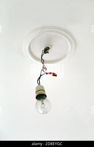 Old incandescent light bulb hanging from the ceiling with the electric wires connected with red tape. White ceiling. Stock Photo