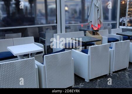 Empty cafe outdoor in a winter day. Coffee shop with armchairs and white sofas in mediterranean style.Outside sun umbrellas are closed for bad weather Stock Photo