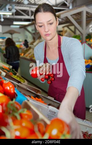 young woman seller showing fresh ripe tomatoes in food store Stock Photo
