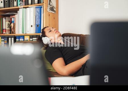 Businesswoman listening music through headphones while lying on sofa at home Stock Photo