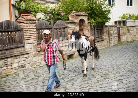 A man talking on a mobile phone leads his horse through the cobblestone streets of Mtskheta, Georgia, Caucasus, Eastern Europe. Stock Photo