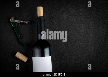 A bottle of red wine, corkscrew and wine corks on black Background, copyspsce. Winemaking  concept Stock Photo