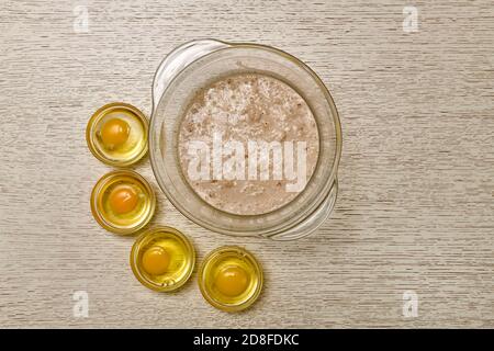 A bowl of fermented bubbling yeast in milk and four cooked nearby broken eggs, each in a small separate cup. Stock Photo