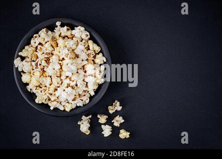 Scattered salted popcorn in a bowl  on black background with copy space. Homemade Popcorn  Top view. Stock Photo