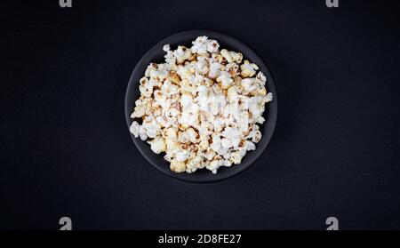 Scattered salted popcorn in a bowl  on black background with copy space. Homemade Popcorn  Top view. Stock Photo