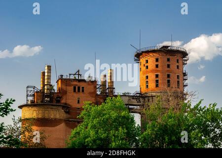 abandoned industrial structures made of bricks, with lightning rods and rusty chimneys against a blue sky with cumulus clouds Stock Photo