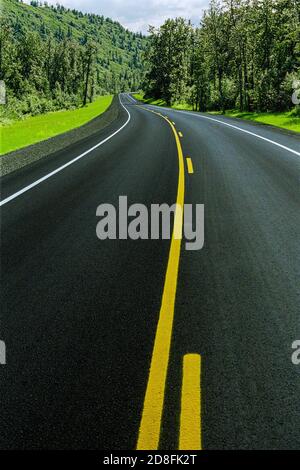 A gently curving road with no traffic winding through forested green mountains. Stock Photo