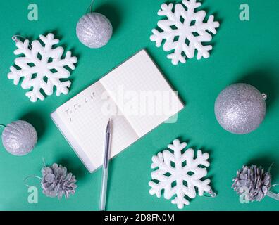 Blank notepad for writing a to-do list, pen, Christmas silver balls, white snowflakes, pine cones on a green background Stock Photo