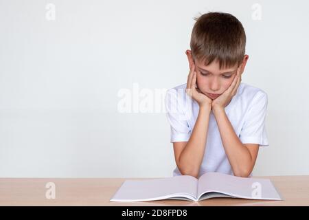 Back to school. Thinking child boy looking in a notebook or book, sitting at the table and doing homework Stock Photo