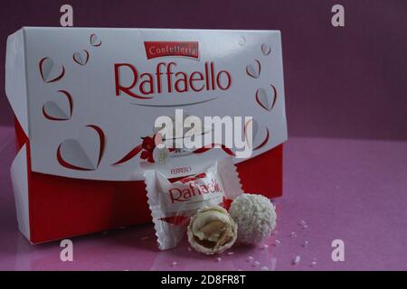 white candies round and halves in the background is a square rectangular gift box Raffaello stands on a pink fuchsia background side view of copy spac Stock Photo