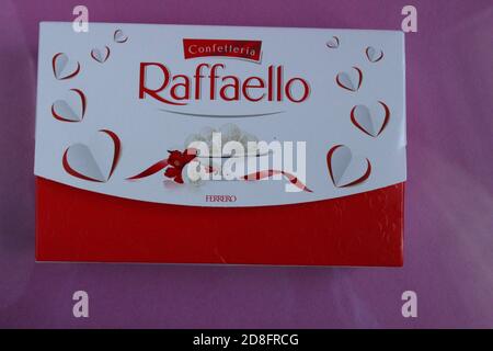white candies round and halves in the background is a square rectangular gift box Raffaello stands on a pink fuchsia background side view of copy spac Stock Photo