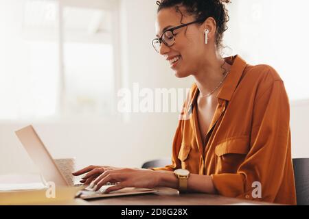 Woman blogger using laptop at home. Woman sitting at table working on her laptop computer and smiling. Stock Photo