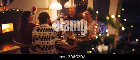 European family sitting at dinner table toasting wine on Christmas eve. Family having thanksgiving dinner at home. Stock Photo