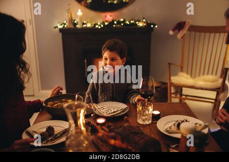 A boy sitting at dinner table on Christmas eve and looking at her mother. Kid having Christmas dinner with family. Stock Photo