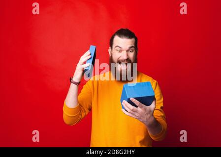 Photo of young bearded man in yellow sweater looking amazed at his gift. Stock Photo