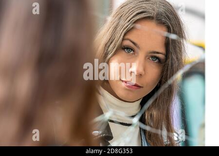 a young, positive woman looks at her reflection in a broken mirror Stock Photo