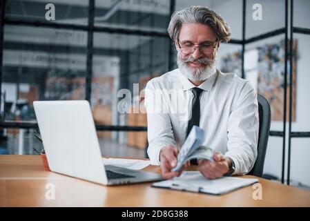Mature businessman with grey hair and beard in formal clothes holding money in hands Stock Photo