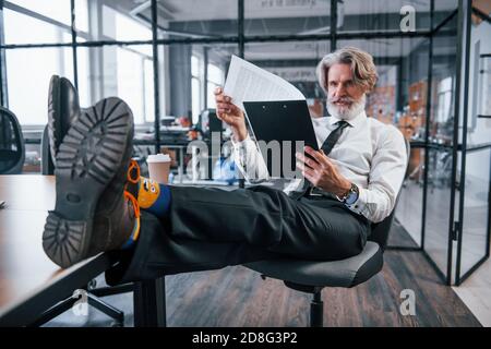 Reading documents. Mature businessman with grey hair and beard in formal clothes is in the office Stock Photo