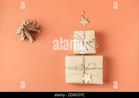 Two Christmas presents wrapped in craft paper lie in form of Christmas tree with wooden star on terracotta background. Copy space. Top view. Stock Photo