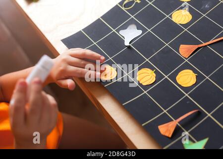 Preschooler boy making board game field for Halloween game, child sticks paper pumpkin Stock Photo