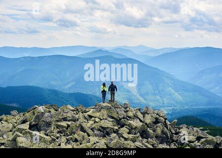 Back view couple tourists holding hands and enjoying powerful view. Man and woman is standing on top of cliff under the sky with cumulus clouds Stock Photo