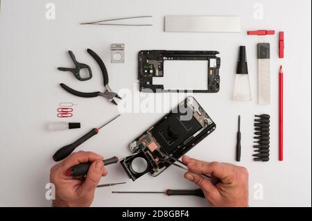 Man working on mobile repair, hands, with tools, screwdrivers, glue, cutting pliers, pencil and red tweezers, white background.Top view, mobile worksh Stock Photo