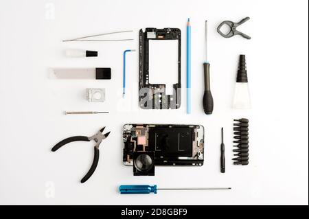 set of objects mobile repair on white background, mobile workshop concept, various tools, broken phone, magnifying glass, glue, screwdrivers, top view Stock Photo