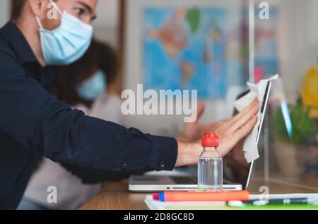 Young man wearing face mask cleaning laptop with sanitizer gel for preventing corona virus spread inside co-working creative space Stock Photo