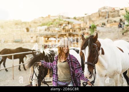 Young smiling farmer taking care of horses inside ranch stable Stock Photo